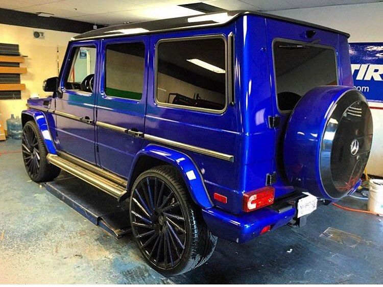Blue Mercedes G-Class SUV with oversized wheels parked indoors, viewed from the rear side.
