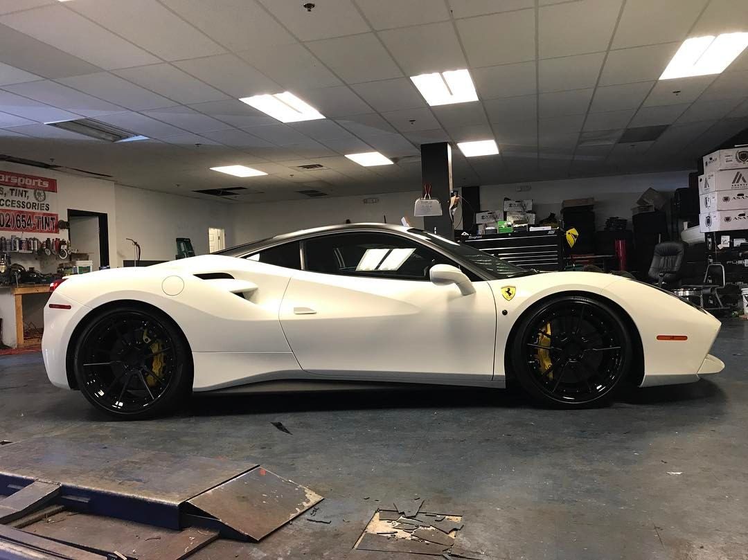 White sports car in a garage, side view, with black wheels and a low profile.