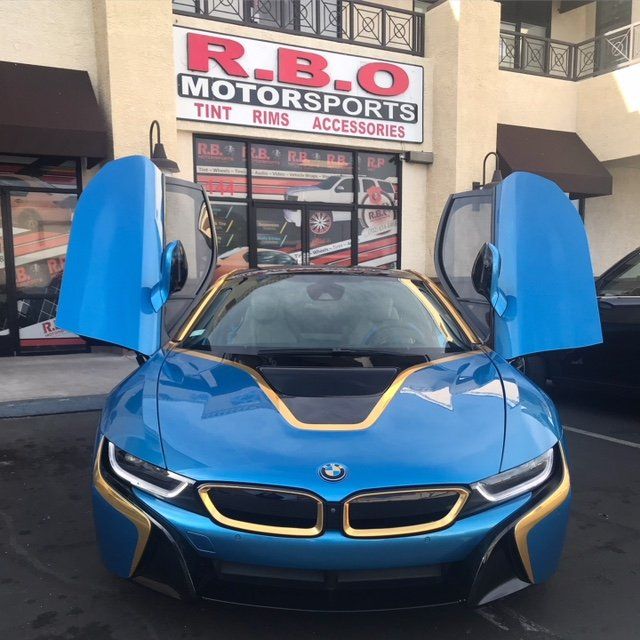 Blue BMW i8 with butterfly doors open outside R.B.O. Motorsports storefront