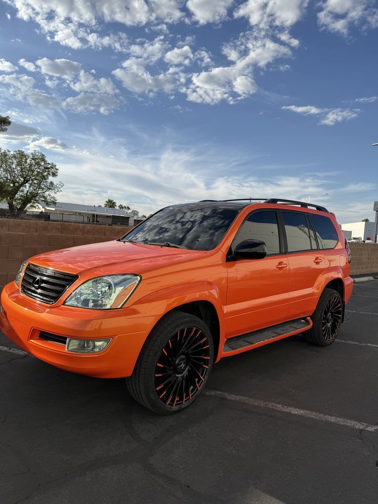 Bright orange SUV with black rims parked in a lot under a blue sky with clouds.