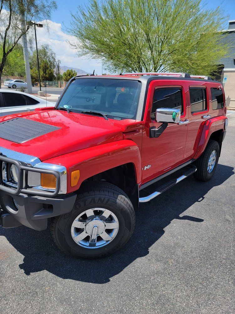 Red Hummer SUV parked outdoors in a sunny lot, with trees and other cars in the background