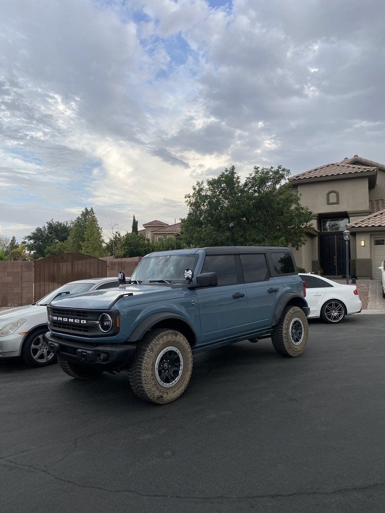 Blue off-road SUV parked on a residential street, with a white car beside it under a cloudy sky.