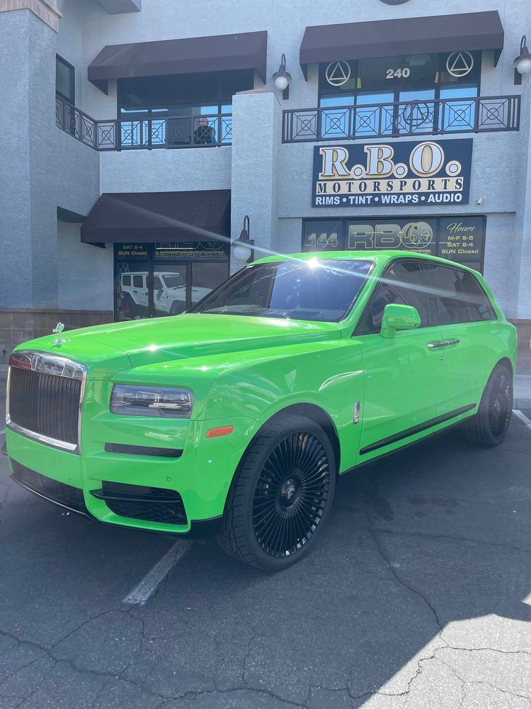 Bright green Rolls-Royce SUV parked outside a building with a salon sign.
