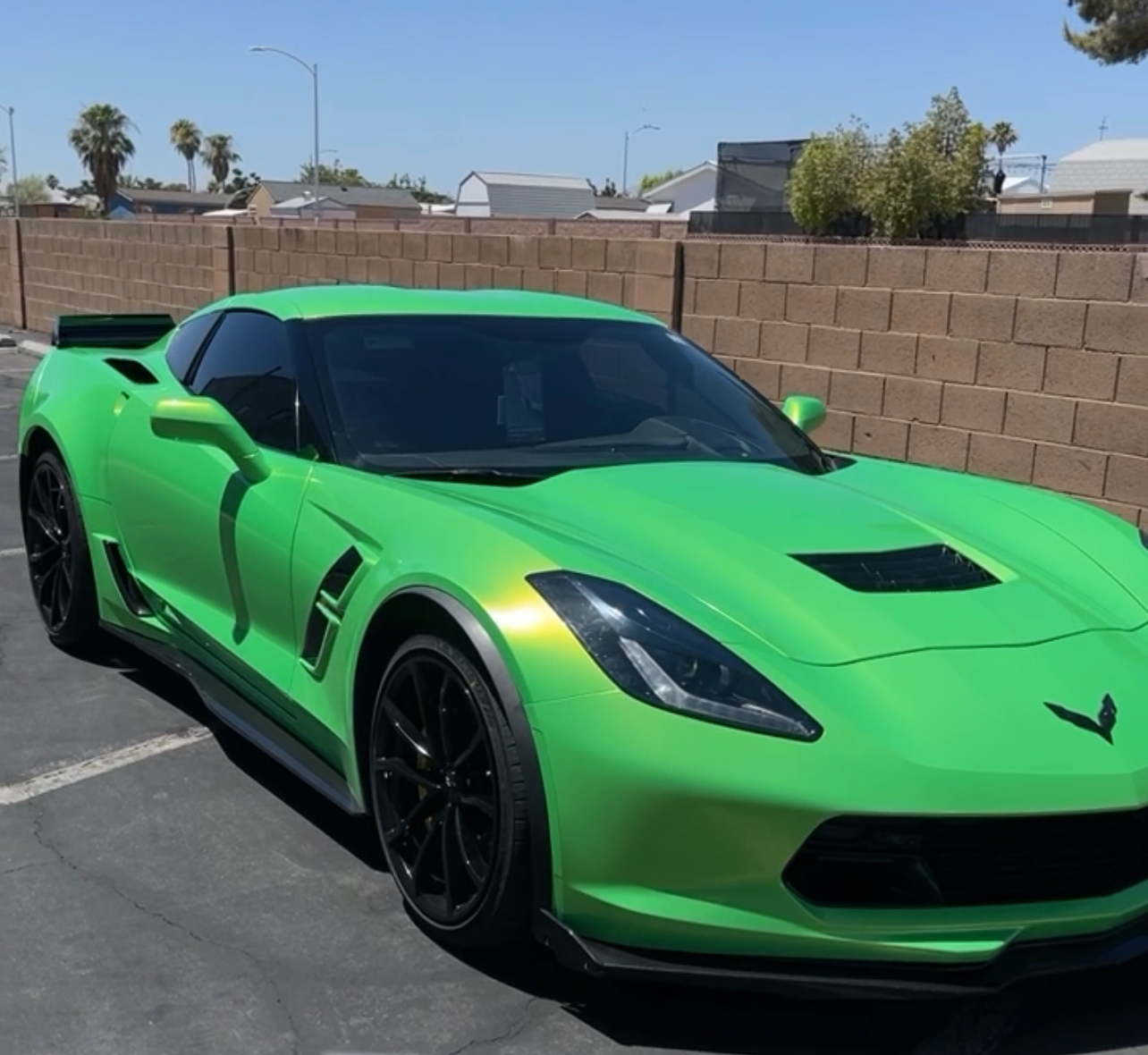 Bright green sports car parked on a sunny street beside a tan brick wall.