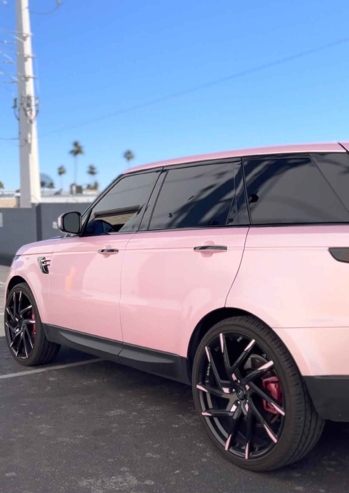 Pink SUV with black rims parked by a roadside under a blue sky