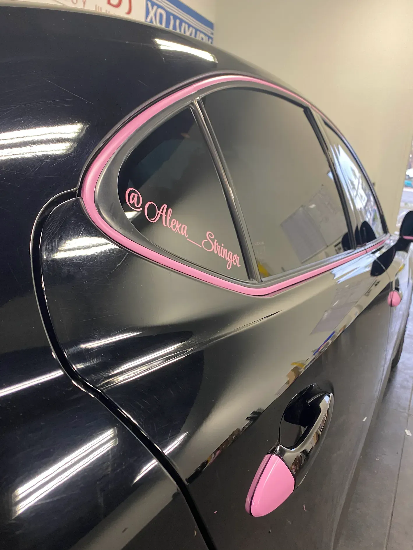Black car side window and door with pink trim and pink accent on the handle, shown indoors.