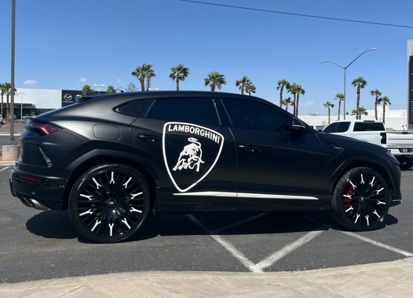 Black Lamborghini Urus with custom black wheels and logo parked outdoors on a sunny street.