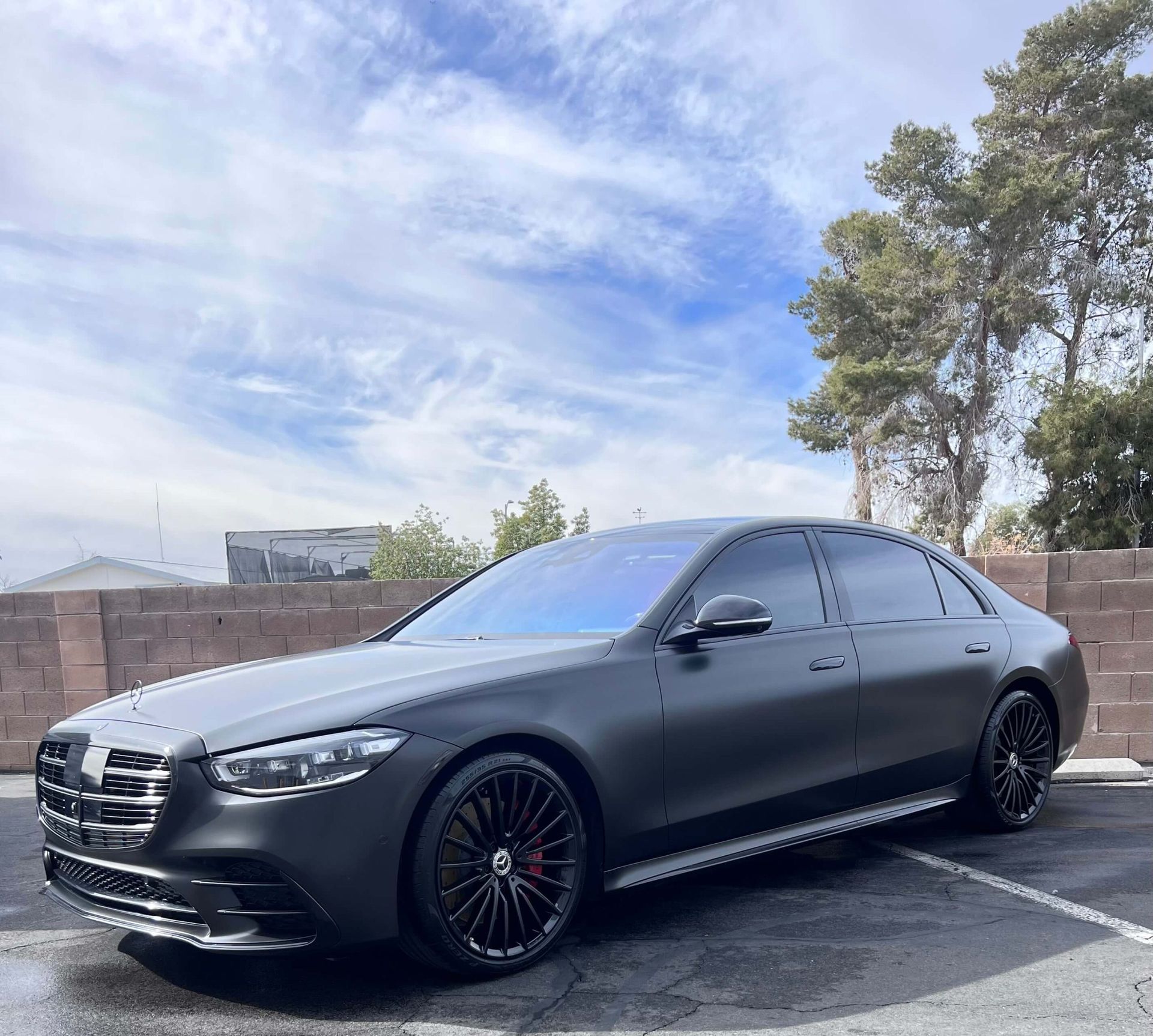 Black luxury sedan parked outdoors under a partly cloudy sky, with a matte finish and tinted windows