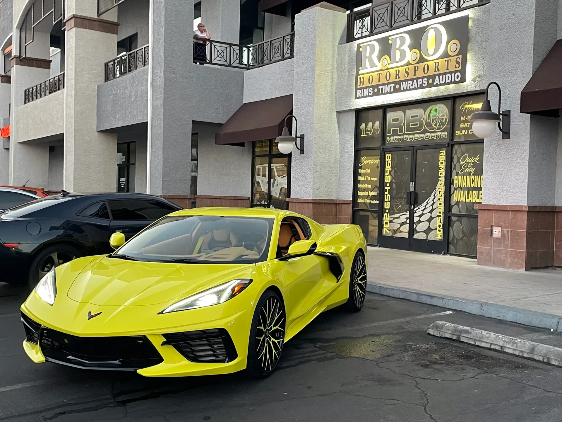 Yellow sports car parked outside a storefront with a black car beside it