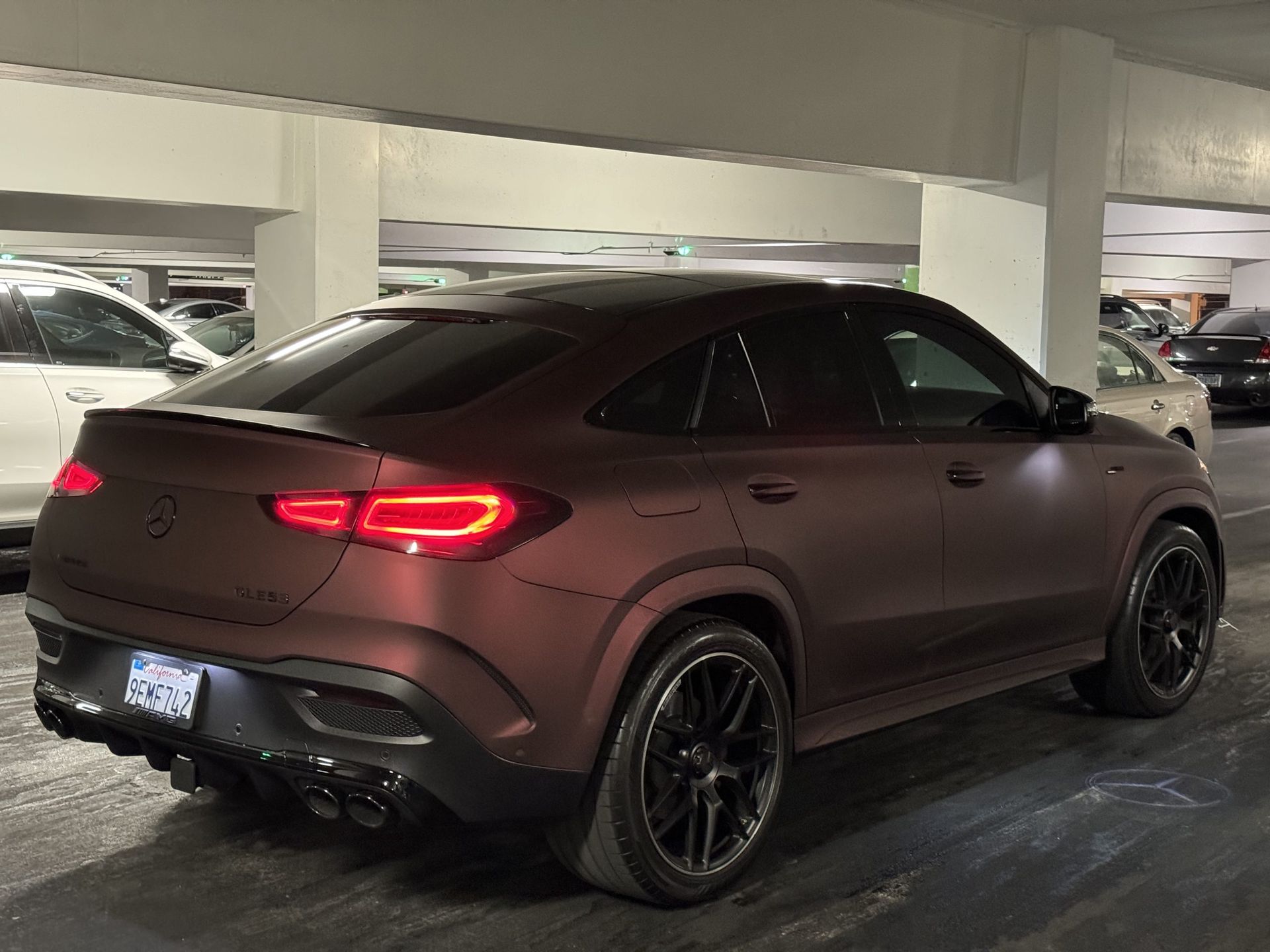 Matte brown SUV parked in a dim garage, rear view with red taillights and black wheels