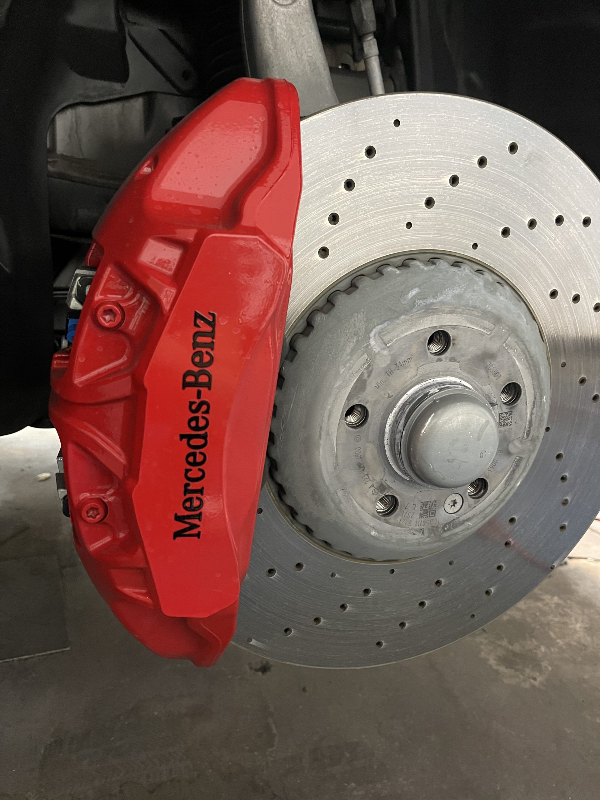 Red Mercedes-Benz brake caliper on a drilled silver brake rotor.