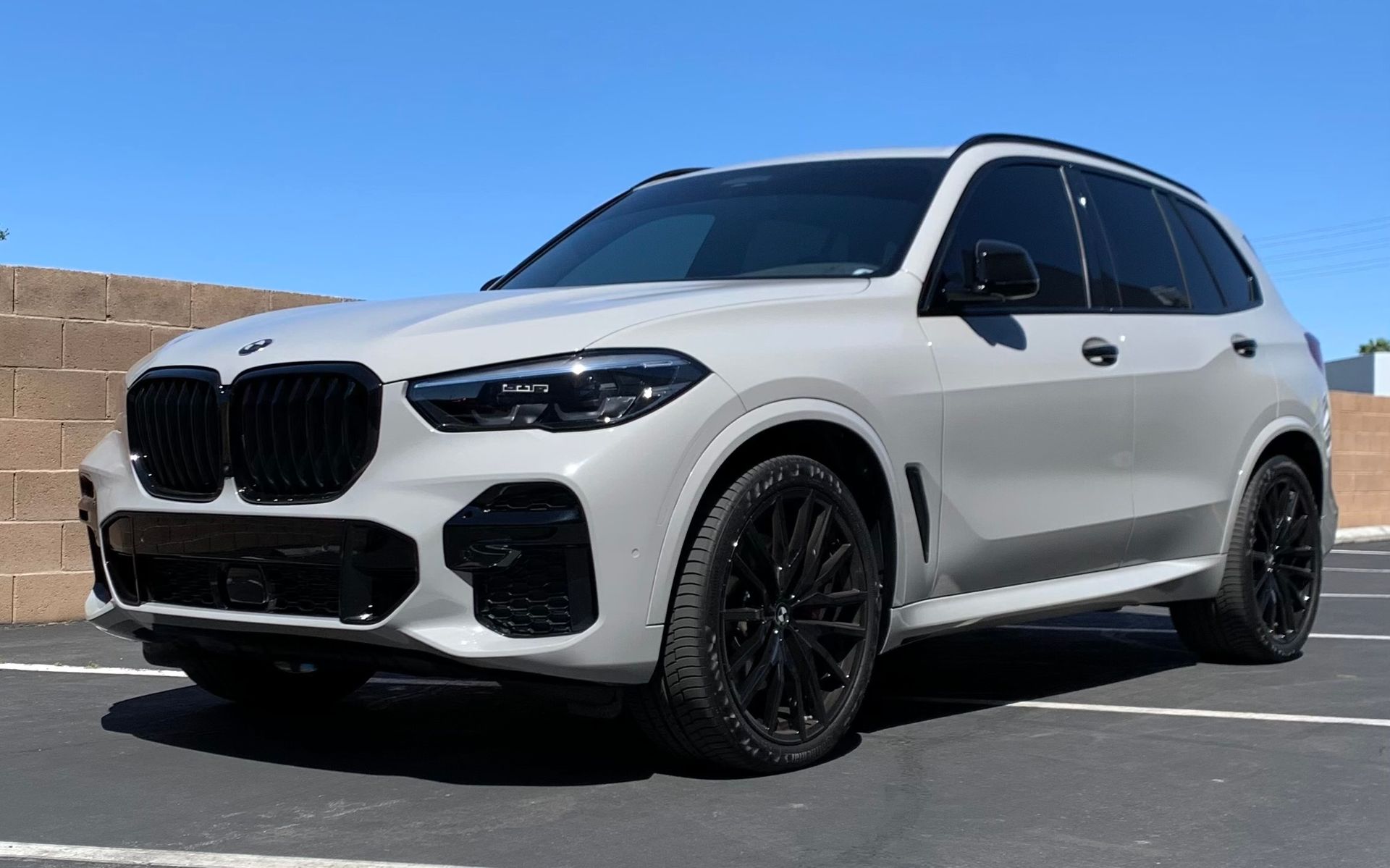 White BMW SUV parked on a sunny road, front three-quarter view with black wheels and tinted windows