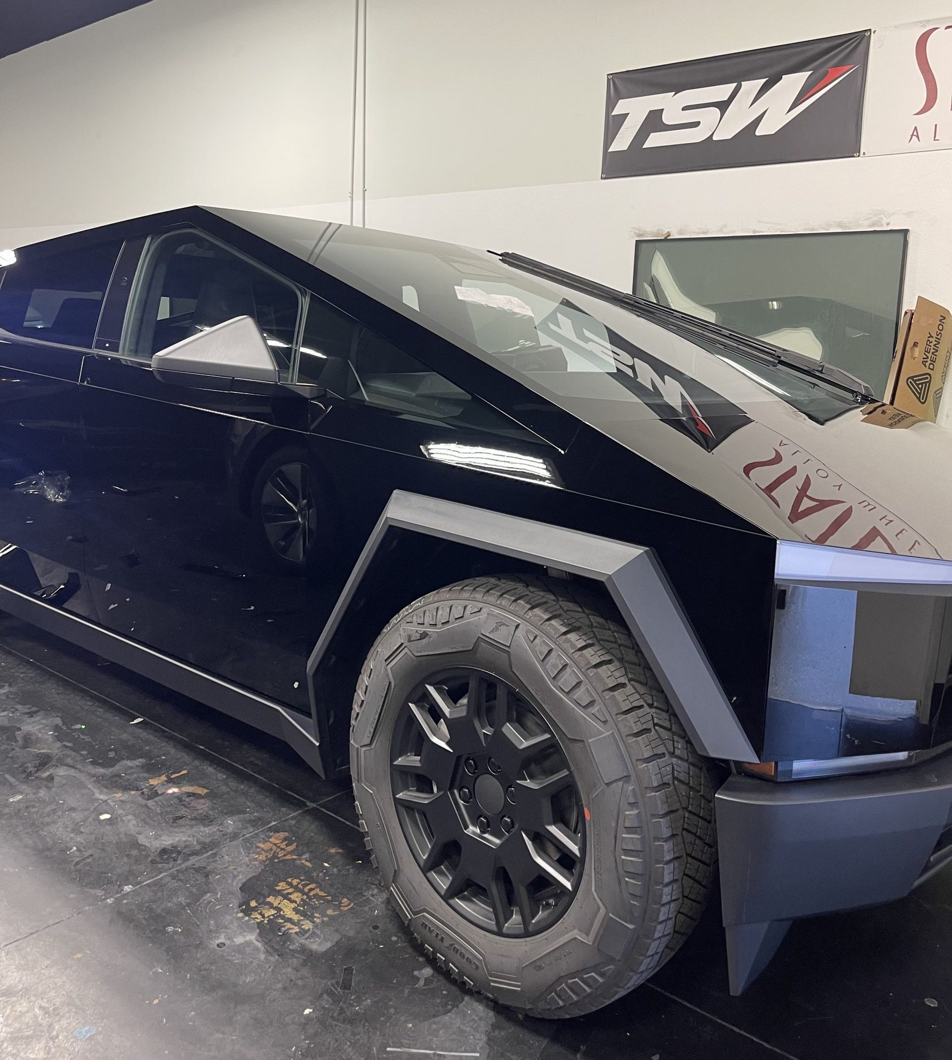 Black pickup truck in a garage, shown front-left with custom wheels and angular body panels