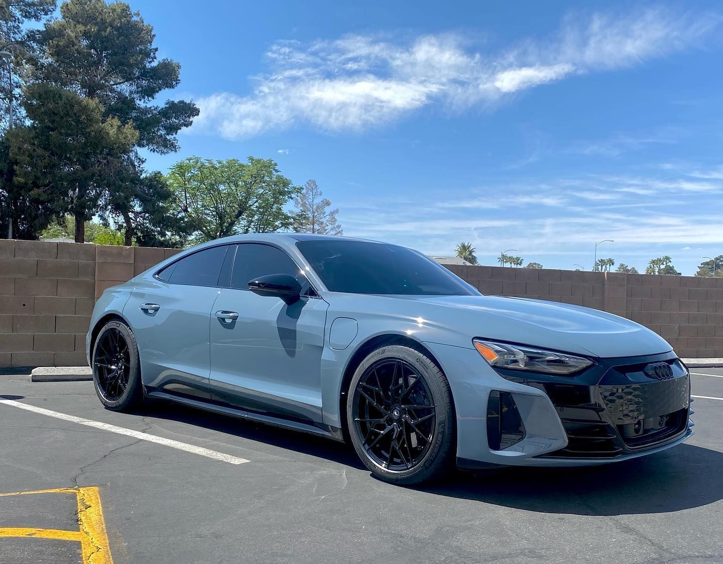 Gray sports coupe parked in a sunny lot beside a tan brick wall under a blue sky