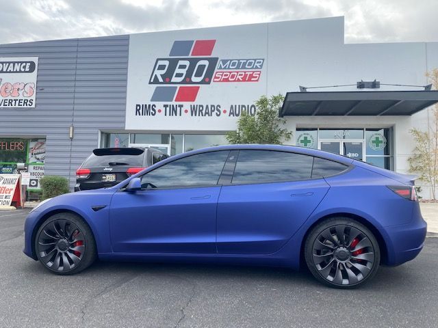 Blue Tesla Model 3 parked outside RBO Motors with aftermarket wheels and tinted windows
