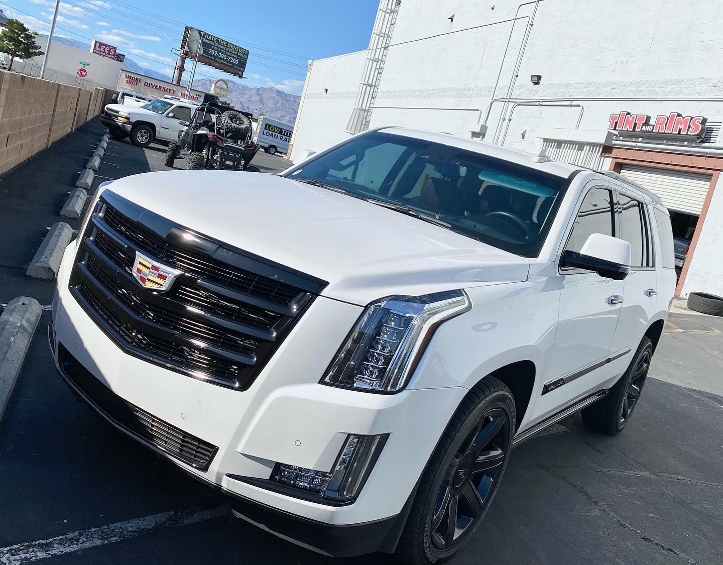 White Cadillac SUV parked outdoors at a car dealership under a clear blue sky