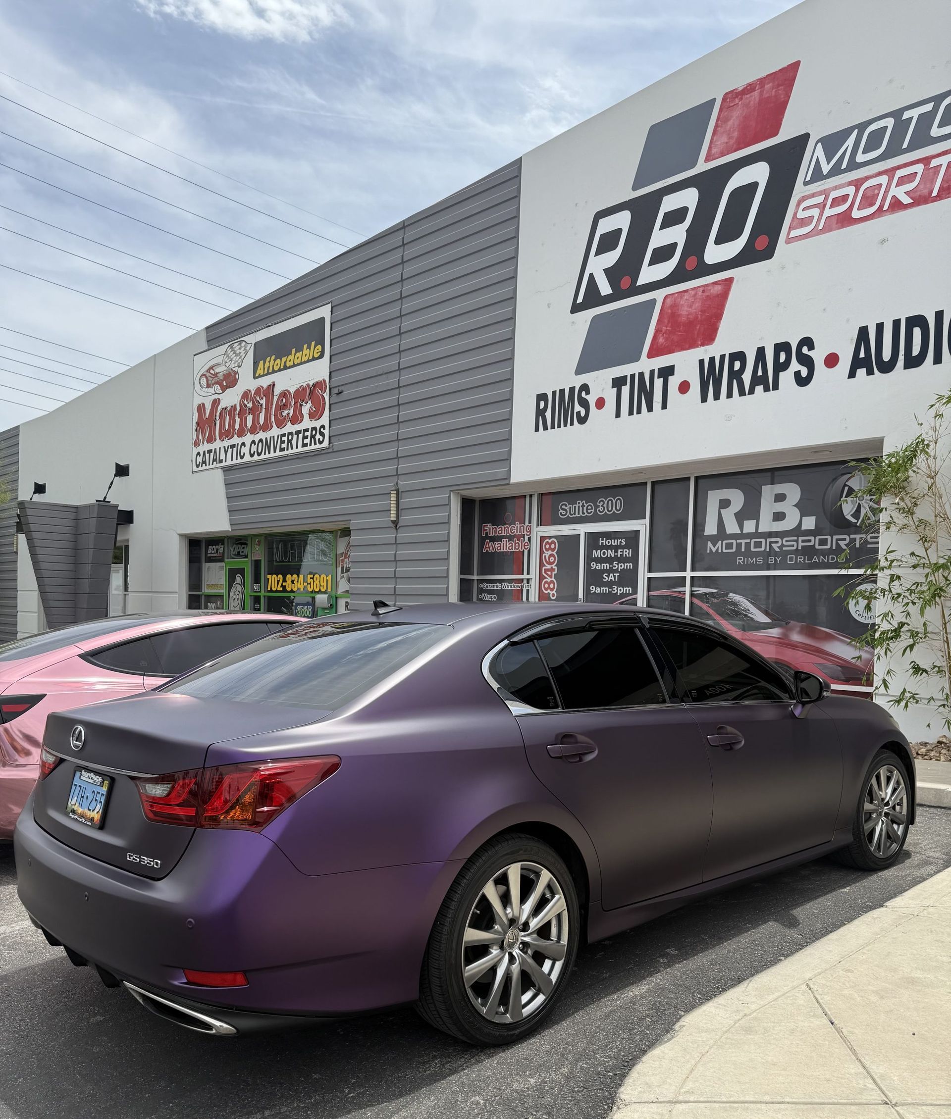 Purple sedan parked outside an auto audio shop with R.B. signs and a gray building facade.