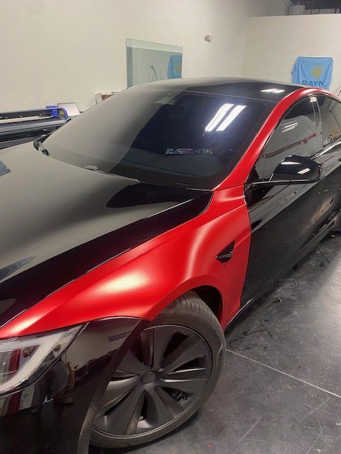 Red and black sports car parked indoors in a garage, with tinted windows and black wheels