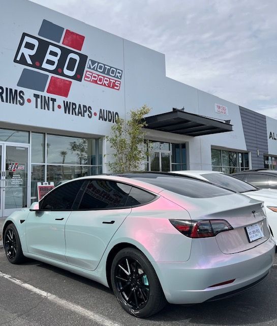 Custom light-blue Tesla parked outside RBO Motor shop with black rims and tinted windows