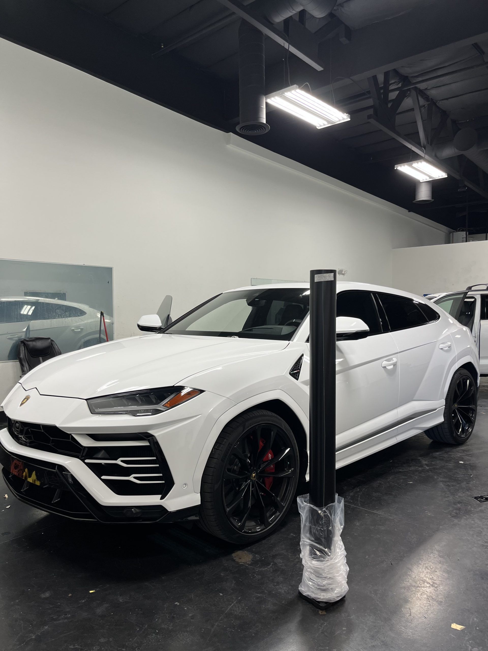White Lamborghini SUV in a showroom, partly blocked by a post, with black wheels and red brake calipers