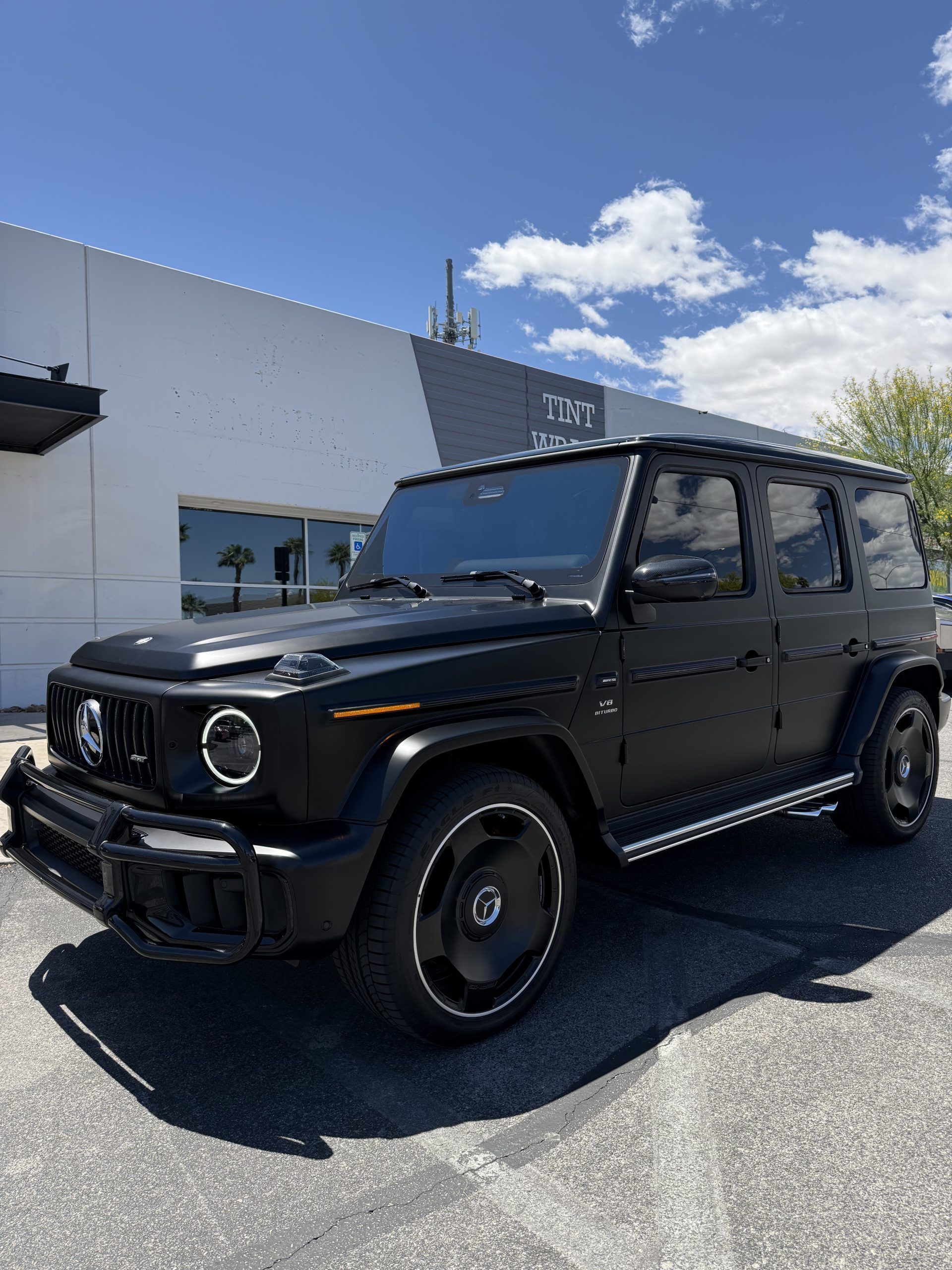 Black Mercedes G-Class SUV parked outside a dealership on a sunny day