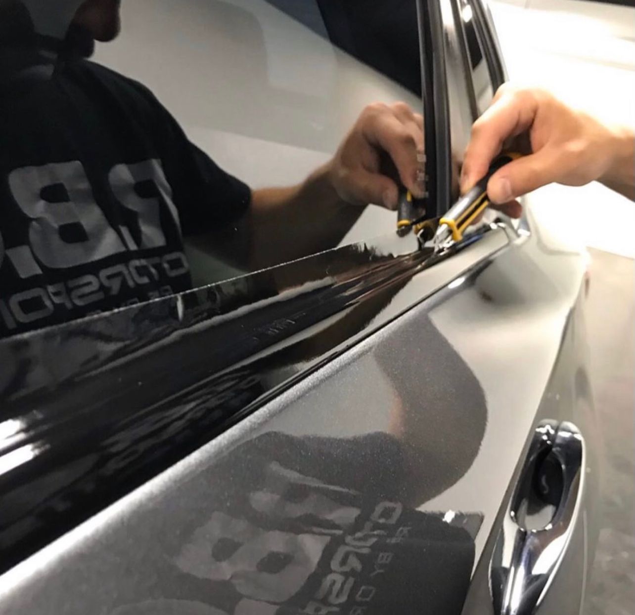 Hand polishing a dark car door with a cloth near the window trim