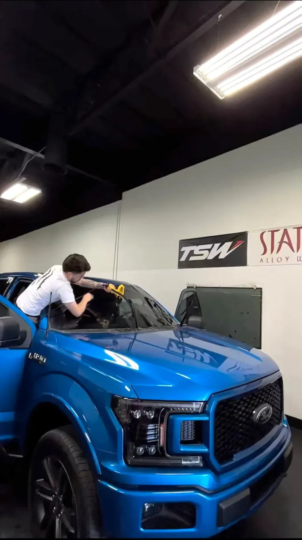 Person polishing a bright blue SUV in a garage with overhead lights