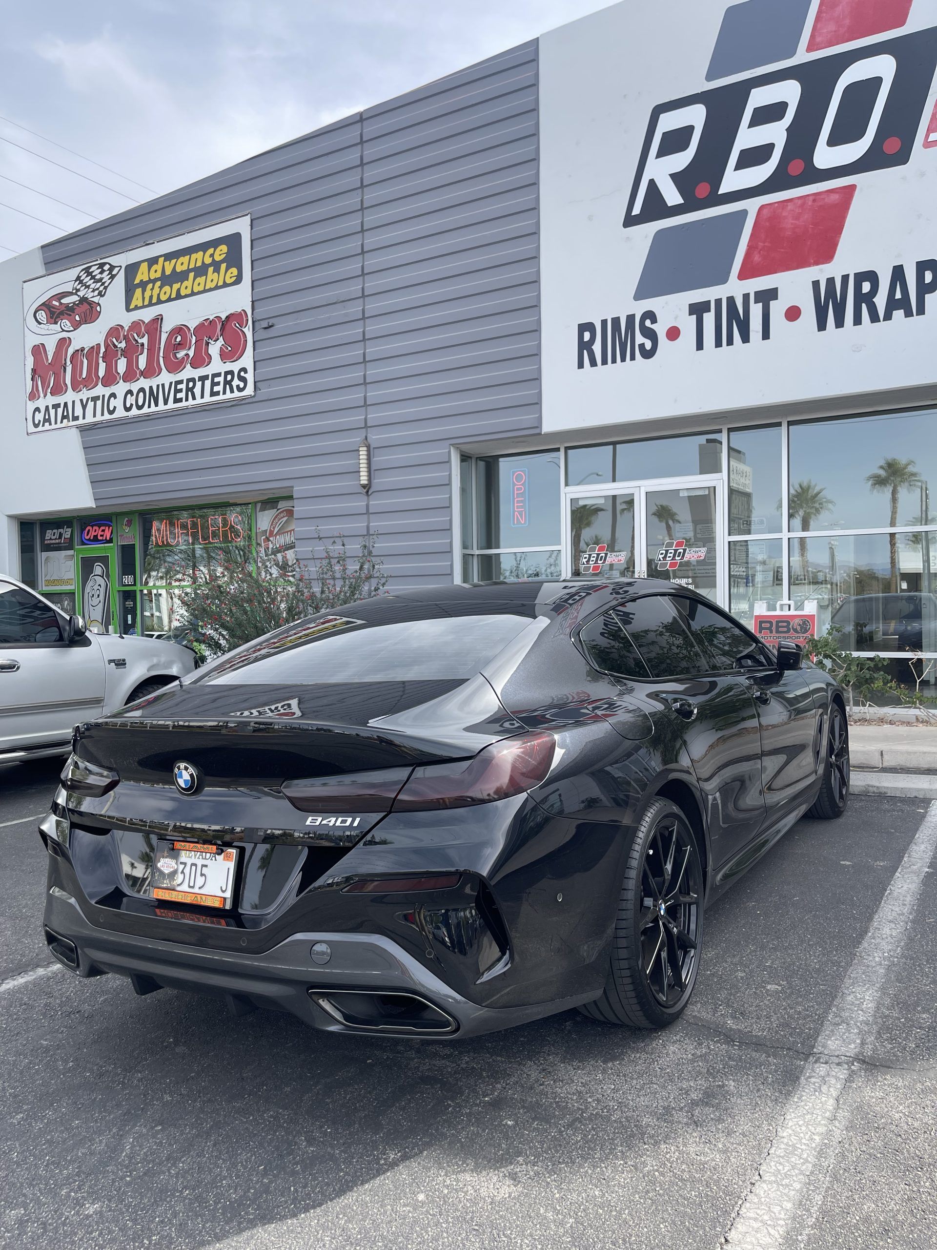 Black sedan parked outside an auto styling shop with sign for rims, tint, and wraps