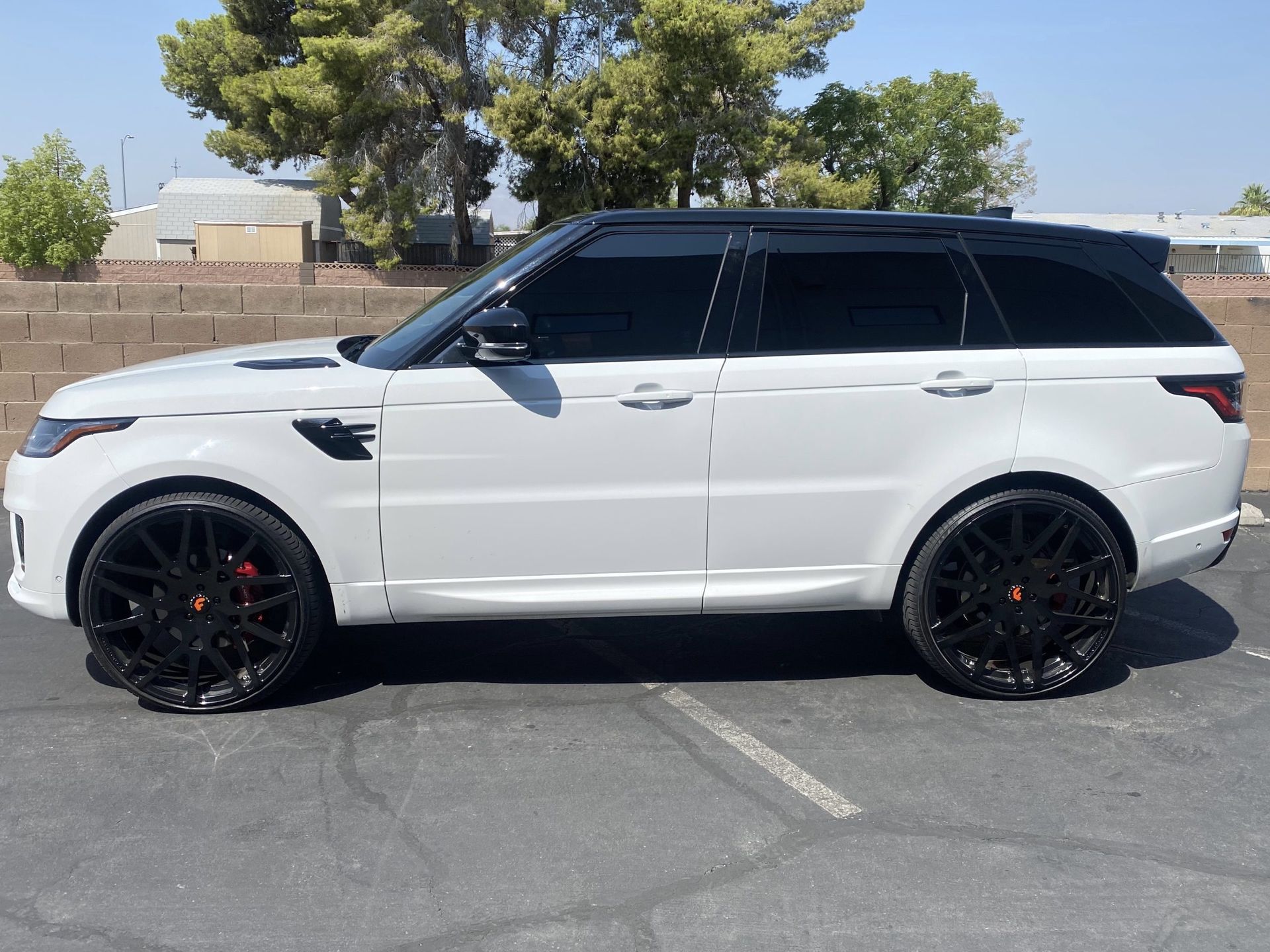 White SUV with black rims parked in a sunlit lot, side view.