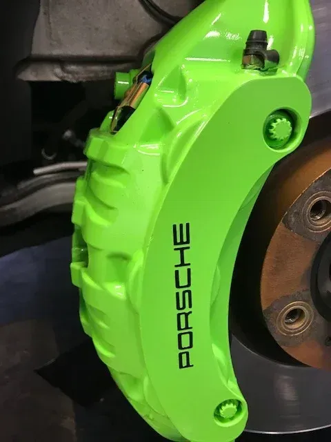 Bright green Porsche brake caliper beside a car wheel rotor