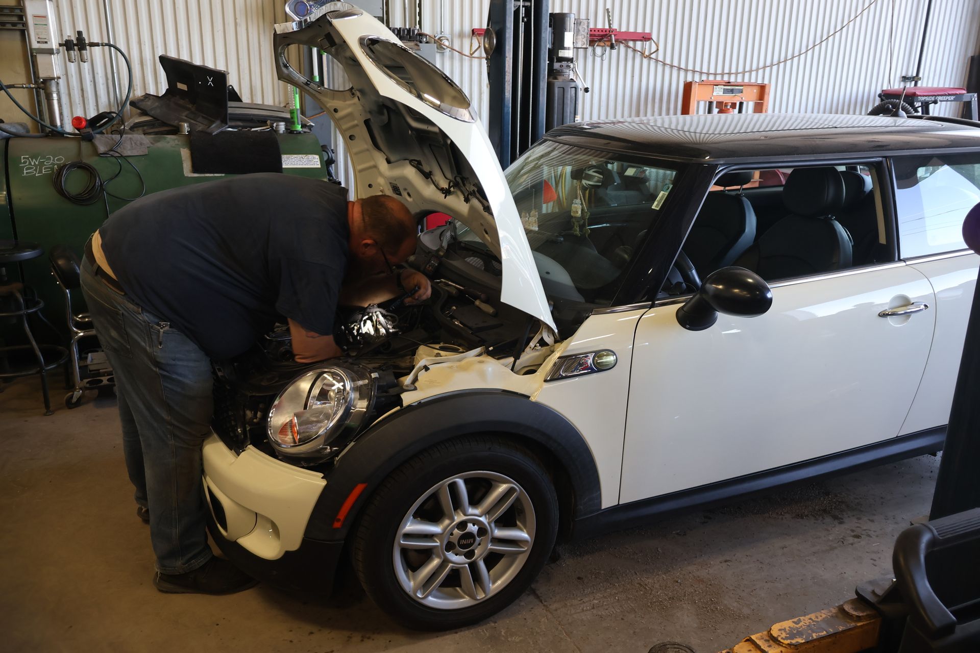 Mechanic working on a white Mini Cooper with the hood open in a garage. | Findlay Auto Plus