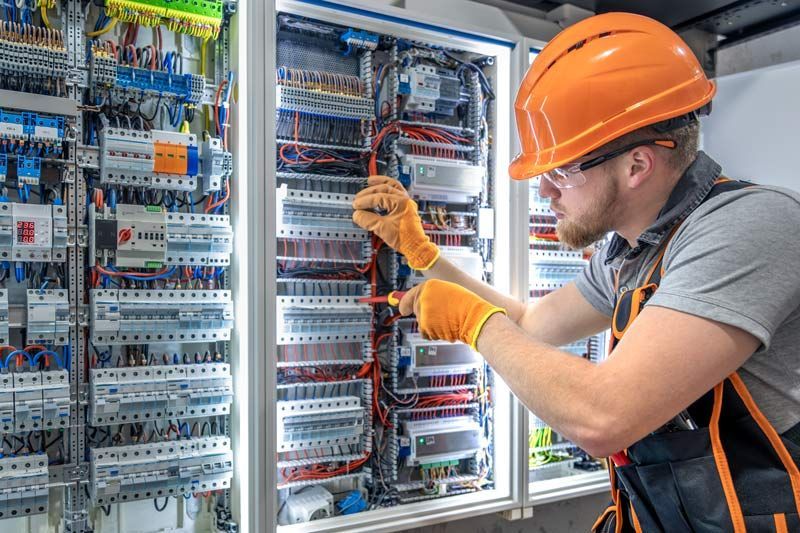 Electrician in orange helmet and gloves working on a complex electrical panel