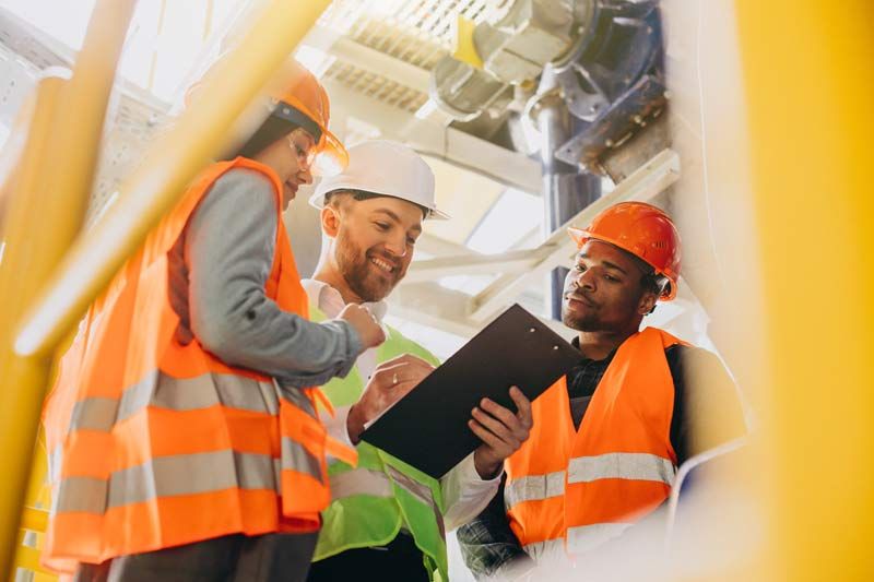 Three workers in safety vests and hard hats reviewing a clipboard