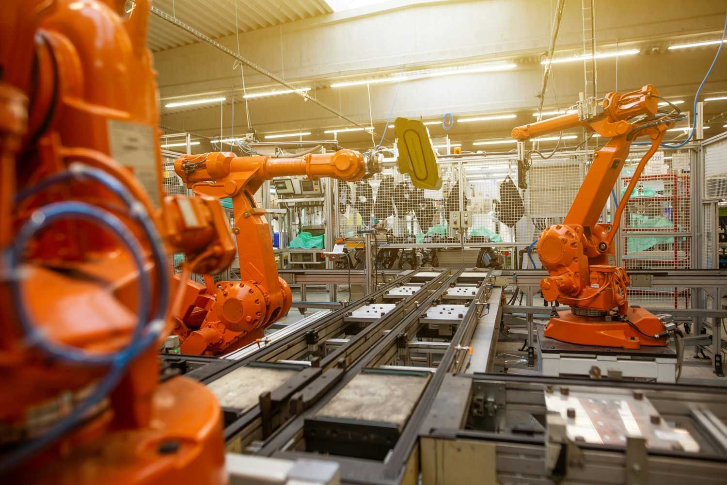 Orange robotic arms working on an assembly line inside a factory