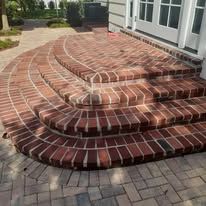 Curved brick front steps leading to a house entrance with white siding and windows