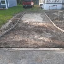 Freshly graded dirt driveway or walkway leading to a house, bordered by curb and grass.