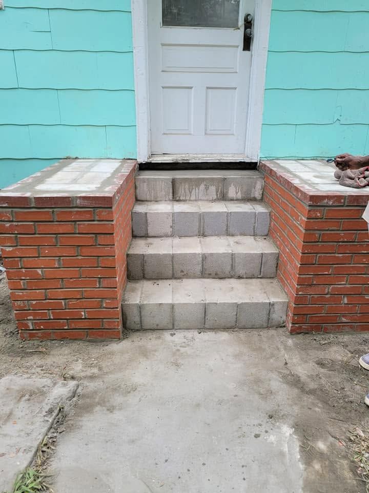 Concrete steps leading to a white door between red brick walls and a turquoise house exterior.