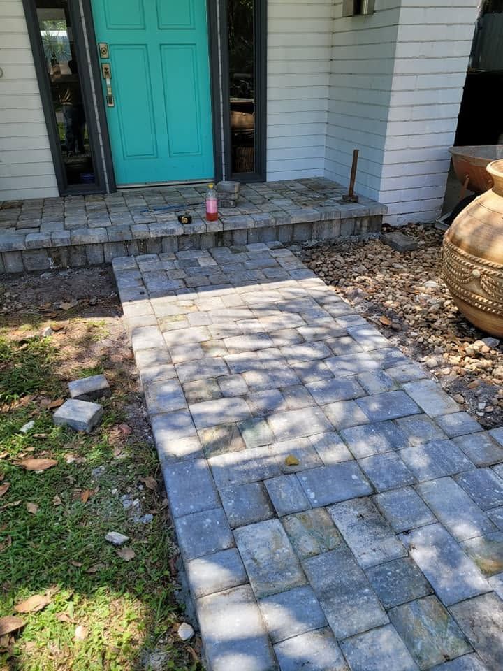 Brick walkway leading to a teal front door with stone steps and porch, dappled sunlight on the path