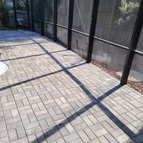 Sunlit brick patio beside a black screened fence, with long diagonal shadows across the ground.