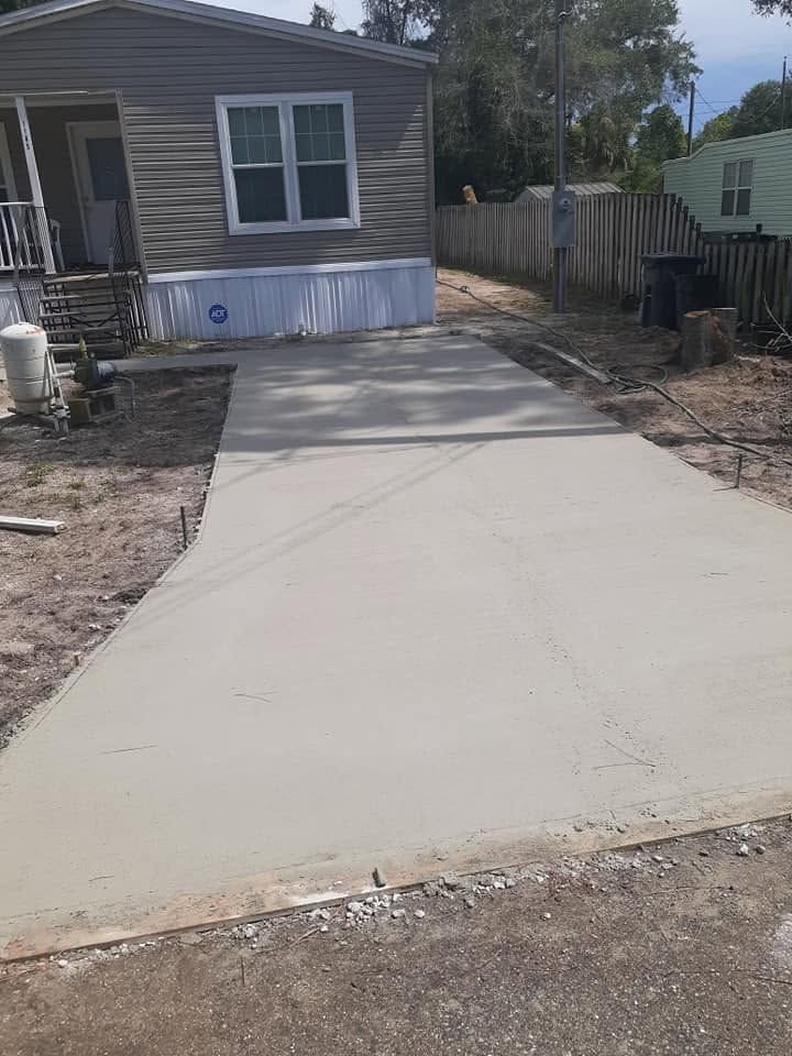 Fresh concrete driveway leading to a gray house with fenced sides and dirt along the edges