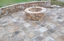 Stone patio with a circular fire pit and curved retaining wall in a backyard