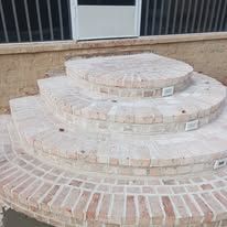 Curved brick steps leading to a raised patio beside a tan wall and metal railing