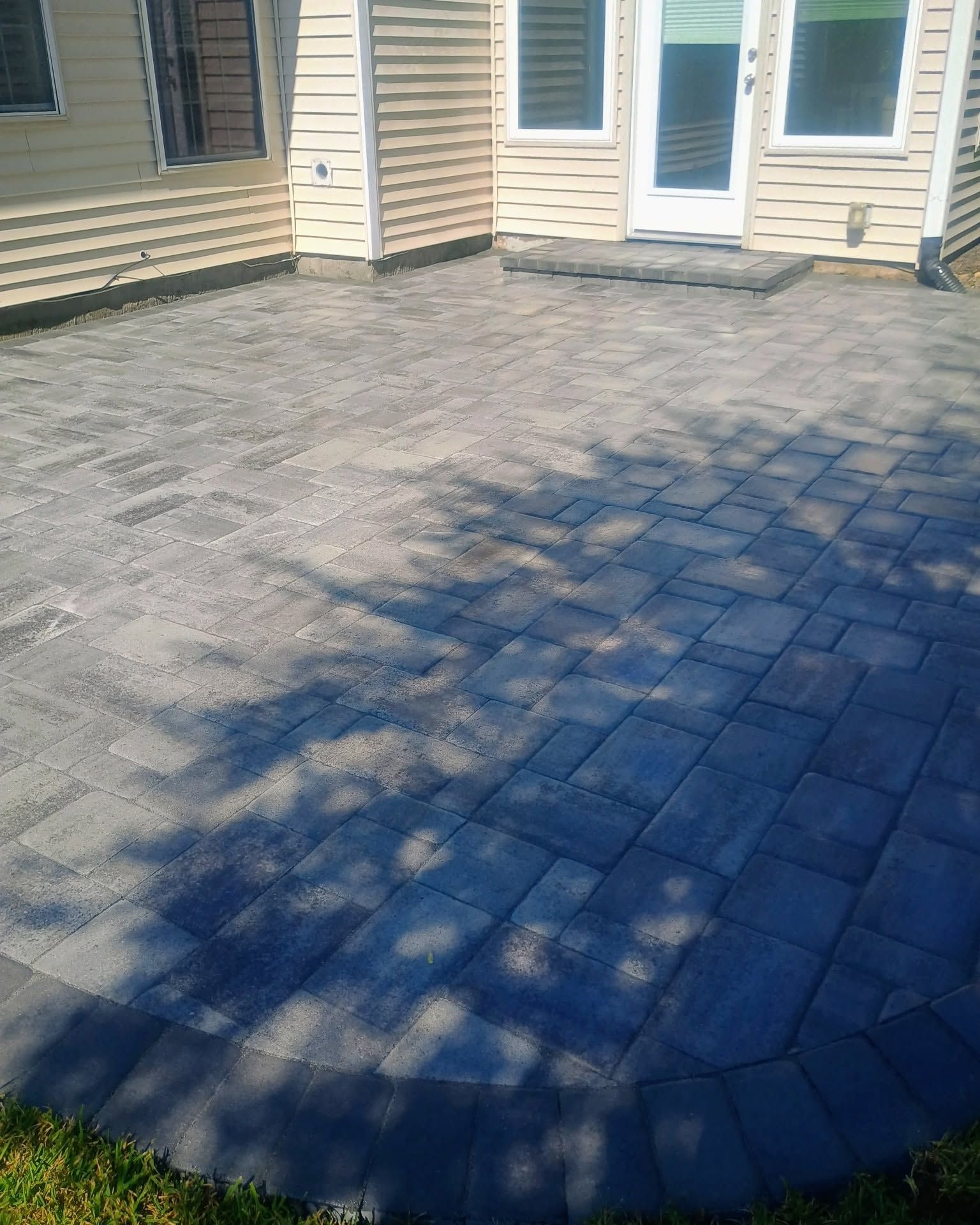 Gray paver patio beside a beige house, with a curved edge and white doors