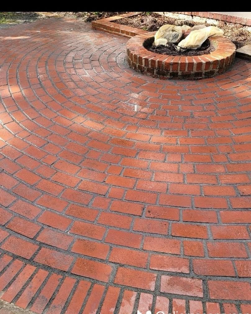 Curved red brick patio with a circular brick fire pit and pale stones in the center