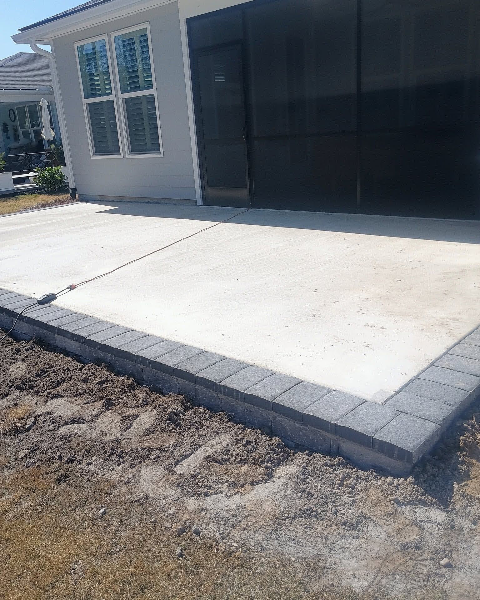 New concrete driveway beside a house, bordered by gray pavers and a black garage door