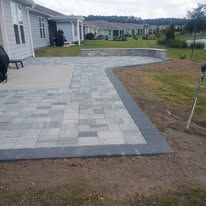 New stone patio walkway beside a gray house, bordered by dark pavers and leading to a yard.
