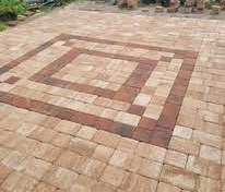 Brick-paved patio with a decorative square pattern in the center and garden items in the background