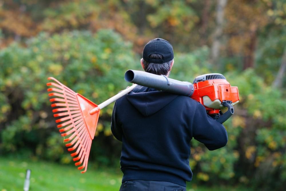 A Man is Carrying a Blower and a Rake on His Shoulder — Gloucester Outdoor Solutions In Gloucester, NSW