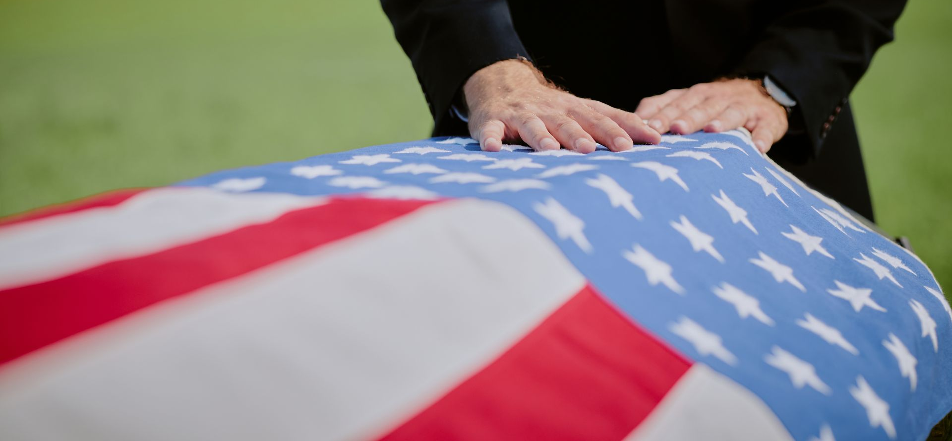 Folded U.S. flag draped over a casket, with hands resting on top