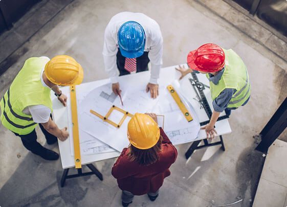 Workers in hard hats reviewing plans around a table at a construction site